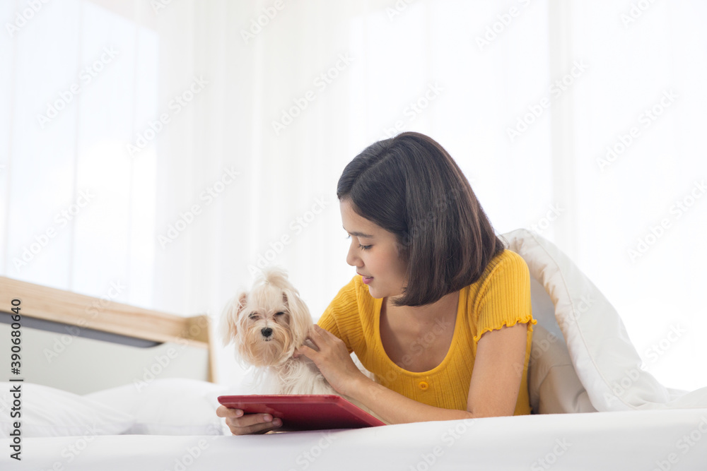 A girl is using a tablet with a maltese dog on a white bed. A girl is using a tablet with a maltese dog on a white bed.
