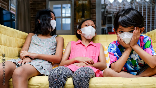 Asian Children Wearing Medical Face Mask Sitting on Sofa Together Feeling Bored During Isolation At Home