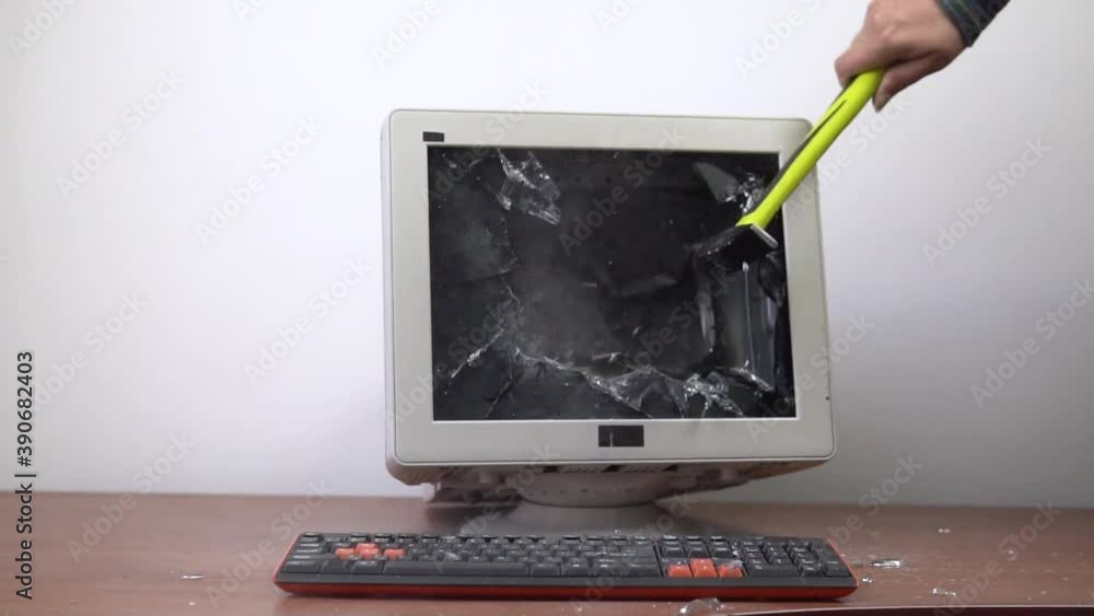 An old monitor sitting on a table is smashed with a hammer. The ...