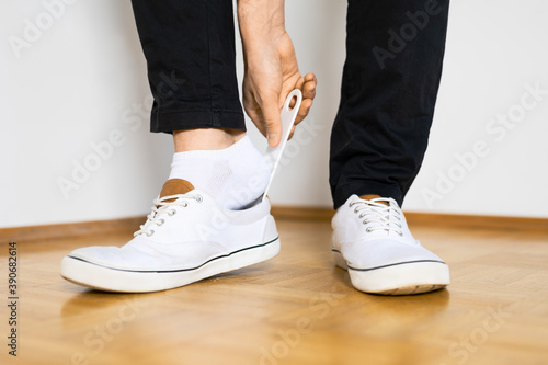 put on shoes with shoespooner on wooden floor by a man with black pants legs