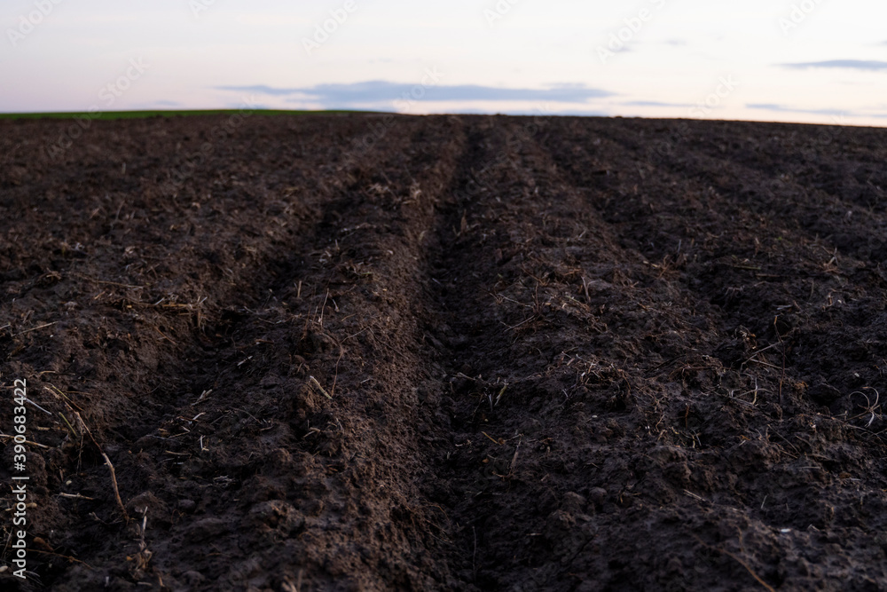 Freshly plowed black rich soil on a field in a sunset.