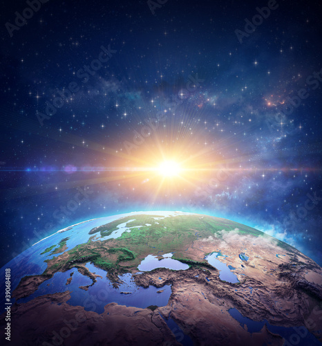Fototapeta Naklejka Na Ścianę i Meble -  Surface of Planet Earth, space view of the World focused on Europe. Rising sun shining into deep space, star cluster and nebula far behind - Elements of this image furnished by NASA