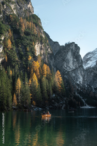 The beautiful, scenic view of fall foliage on the shore of the famous Braies Lake in Trentino Alto Adige, Italy. Water reflections, Doomites in the background and tourists in a row boat.