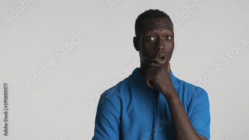 Young amazed African American man thoughtfully rubbing chin looking surprised in camera isolated on white background. Wow face
