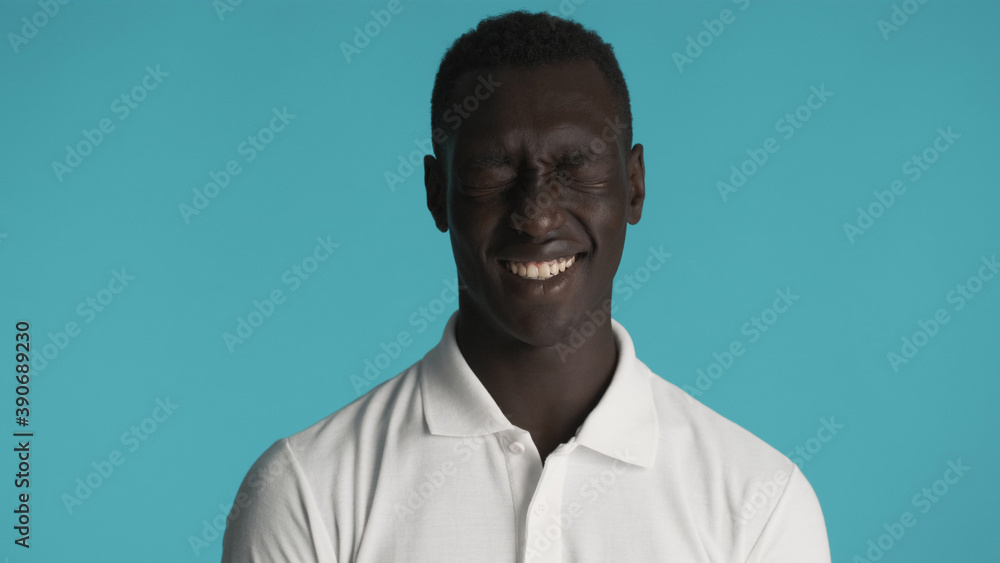 Attractive African American man in white T-shirt joyfully posing on camera over blue background. Happy expression Attractive African American man in white T-shirt joyfully posing on camera over blue background. Happy expression