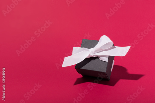Black Friday sale concept. Black color gift box with white ribbon on red background.