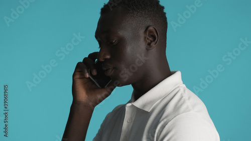Side view of attractive African American guy talking on smartphone isolated on blue background