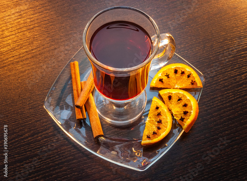 Obraz na płótnie Tea in a glass cup on a saucer next to orange slices with cloves and cinnamon sticks. Wooden table as a background w salonie