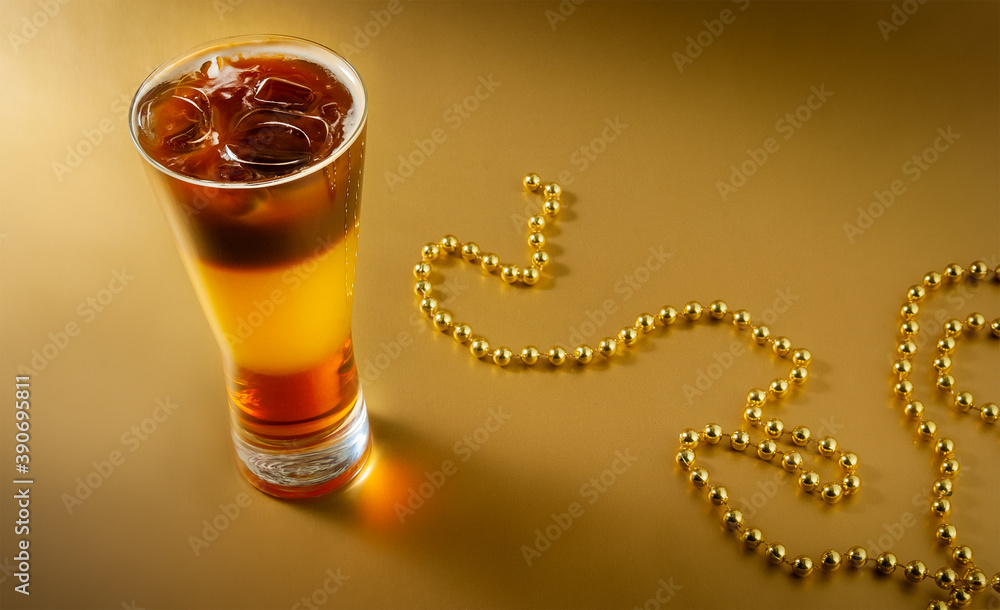 Cold coffee cocktail with layers of liqueur and orange juice with ice on a gold background with pearl beads