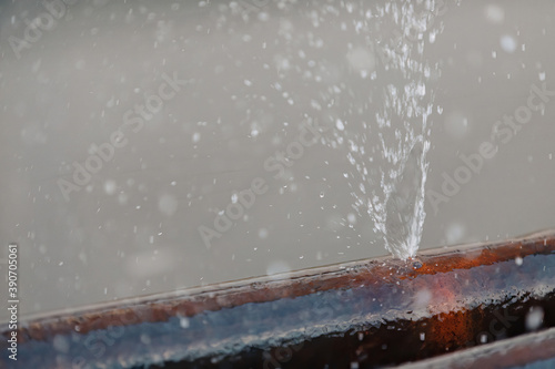 Water splashes from a hole in a metal water pipe.