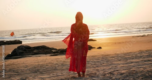 Young women wearing a red saree on the beach goa India.girl in traditional indian sari on the shore of a paradise island among the rocks and sand enjoying the freedom and the sunset photo