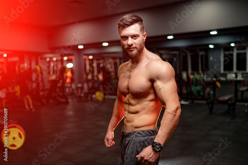 Very muscular sporty guy drinking protein in dark red background with naked torso. Athletic body. Sport and sport nutrition concept.