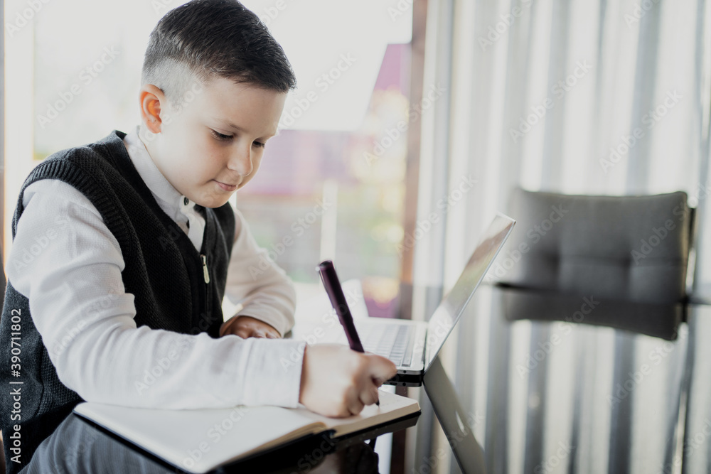 does lessons online with a teacher. schoolboy boy dark-haired European appearance. dressed in a school white shirt and stylish hairstyle holding a laptop. does lessons online with a teacher. schoolboy boy dark-haired European appearance. dressed in a school white shirt and stylish hairstyle holding a laptop.