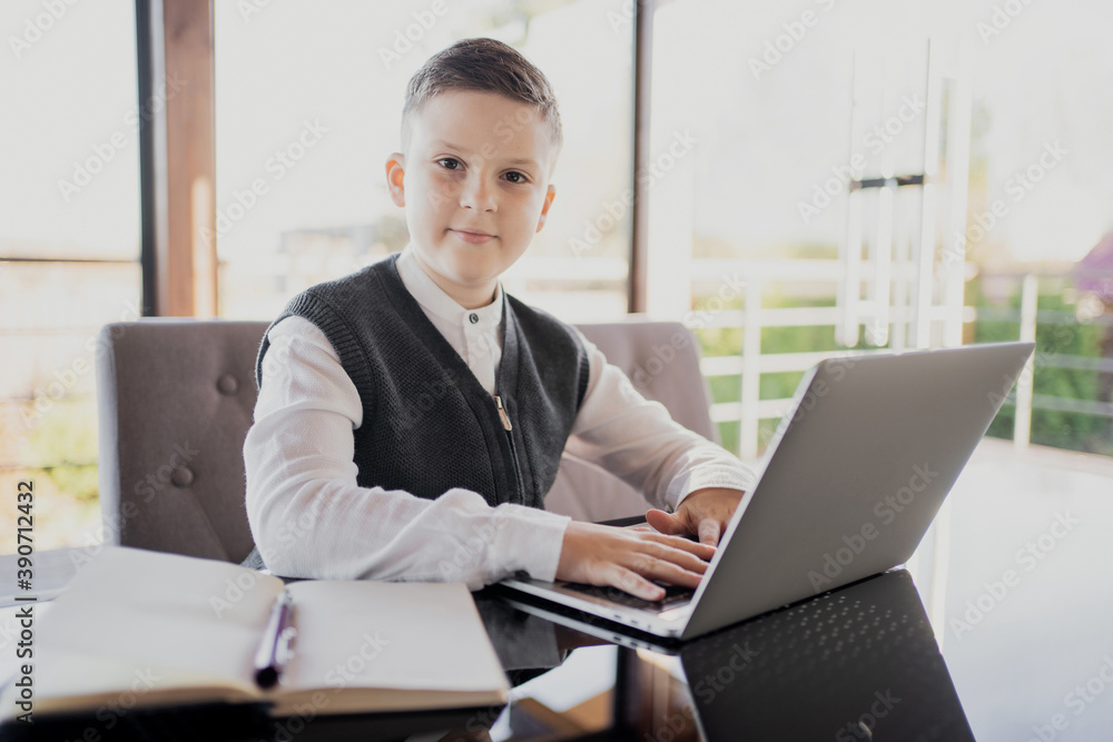 European appearance schoolboy boy dressed in a white shirt, looking at the camera. learning at home online on a laptop video call with an English teacher. European appearance schoolboy boy dressed in a white shirt, looking at the camera. learning at home online on a laptop video call with an English teacher.