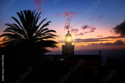 Ponta do Pargo lighthouse, silhouette of a glowing lighthouse against an orange evening sky. Tourist place. Traveling around Madeira island, Portugal