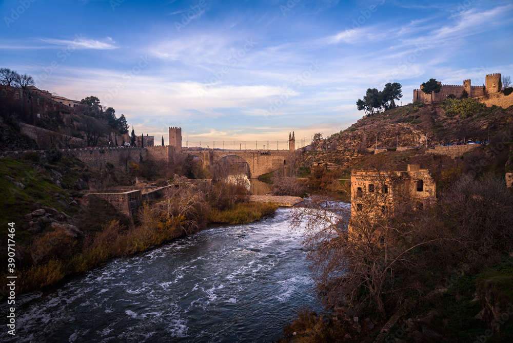 The famous Alcantara bridge over Tagus river and the castle in the medieval city of Toledo at sunset, Spain