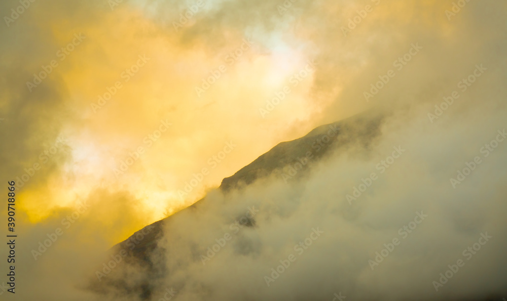 Sunlight breaking through dense storm clouds over a mountain ridge.