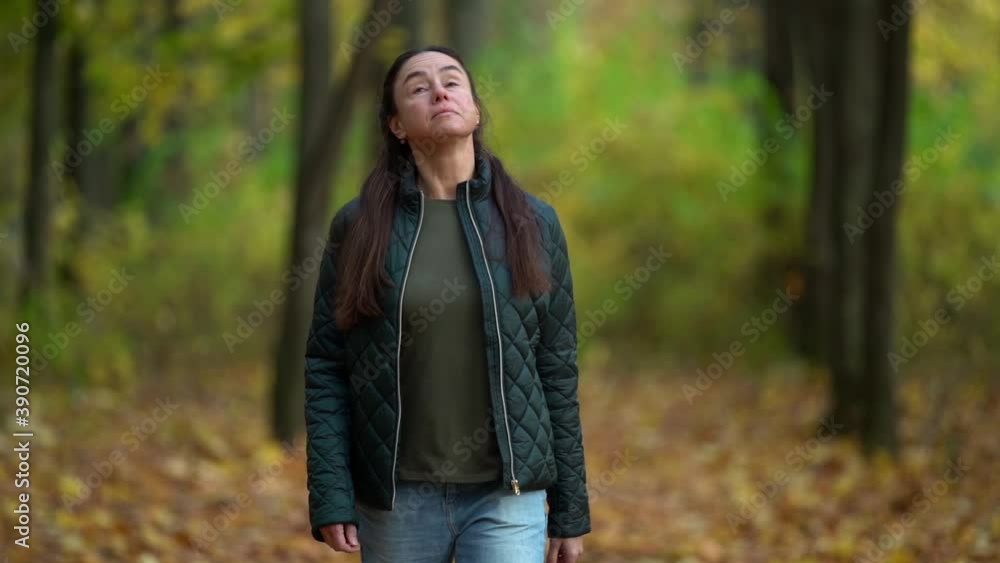 Middle-aged woman with dark hair, enjoying nature in the autumn forest. Walking among the trees in the sunlight. Model in blue jeans and an outdoor jacket. Middle-aged woman with dark hair, enjoying nature in the autumn forest. Walking among the trees in the sunlight. Model in blue jeans and an outdoor jacket.