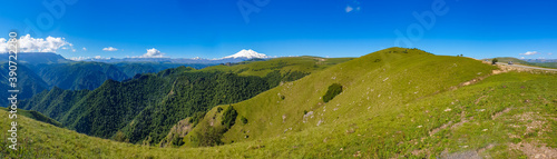 Amazing panorama of caucasian mountain  volcano Elbrus with green fields  blue sky background. Elbrus panorama landscape view