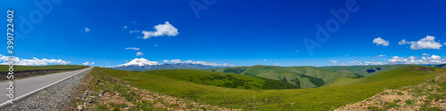 Great nature mountain range. Panorama perspective of caucasian mountain or volcano Elbrus with green fields  blue sky background. Elbrus landscape view - the highest peak of Russia and Europe