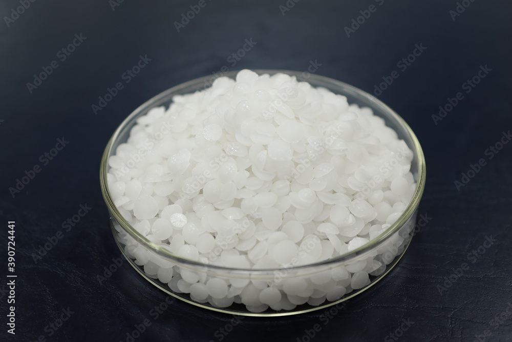 Selective focus of sodium or potassium hydroxide white chemical compound pellets or prills in a petri dish in black background. Selective focus of sodium or potassium hydroxide white chemical compound pellets or prills in a petri dish in black background.