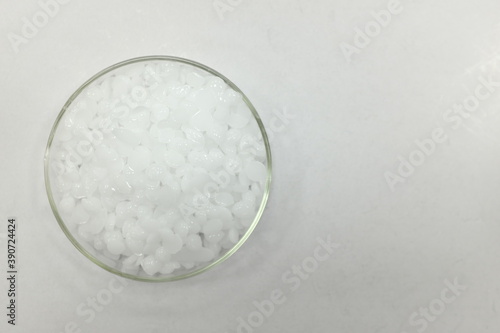 Top view of sodium or potassium hydroxide white chemical compound pellets or prills in a petri dish in white background.