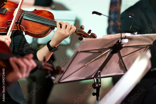 Symphony music. Woman playing the violin in orchestra near music note stand