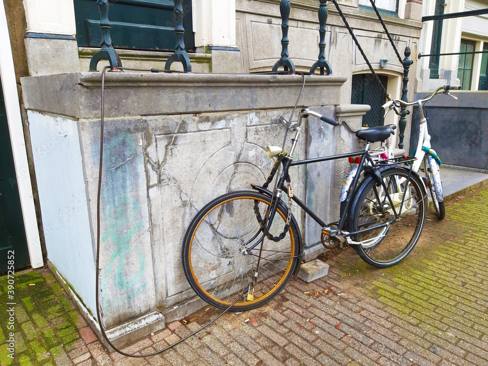 Dutch bicycles parked abandoned on the wall of a house with the anti theft security chain along the sidewalk