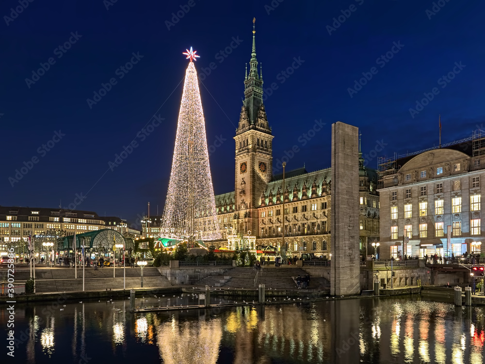 Hamburg, Germany. Christmas market with large illuminated Christmas tree at Town Hall square in front of Hamburg Town Hall in dusk. View from Alsterarkaden at Kleine Alster river.