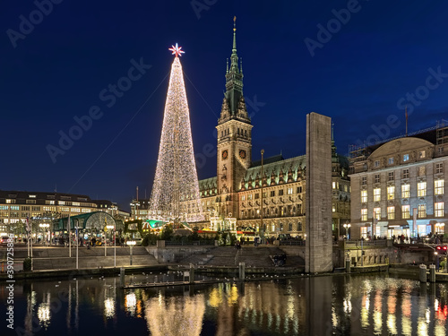 Hamburg  Germany. Christmas market with large illuminated Christmas tree at Town Hall square in front of Hamburg Town Hall in dusk. View from Alsterarkaden at Kleine Alster river.