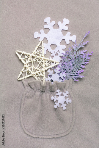 Fototapeta Naklejka Na Ścianę i Meble -  Happy New Year composition in the pocket of a gray fleece jacket. Christmas or winter still life made of snowflakes, handmade star and cypress branch on gray background. Flat lay, top view.