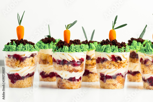Macro shot of the trifle with carrot shaped marzipan and grass decoration on top. Layered dessert in a glass on the white background.