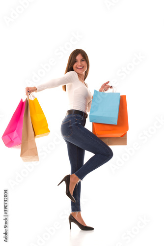 Beautiful girl with purchases in her hands smiling at the camera. Brunette stands on white background with purchases after sale. 