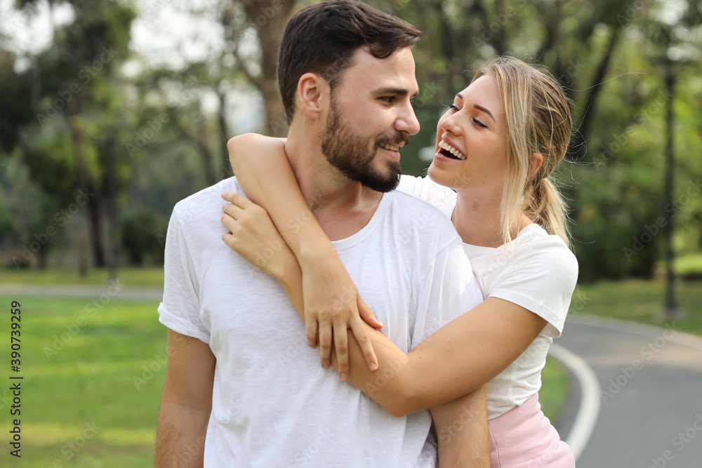 Young caucasian girl wearing white T-shirt standing and hugging her boyfriend with happy smiling face in park outdoor during summer season. (healthy or friendship concept) Young caucasian girl wearing white T-shirt standing and hugging her boyfriend with happy smiling face in park outdoor during summer season. (healthy or friendship concept)