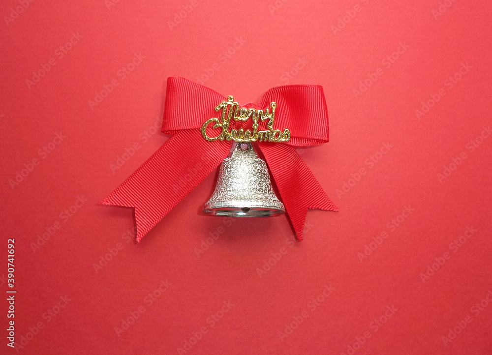 Red bow with the inscription merry Christmas and a silver bell on a red background.