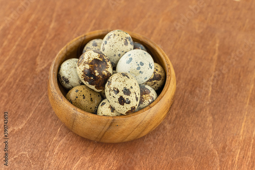 fresh quail eggs speckled white and dark in a wooden bowl on a wooden background