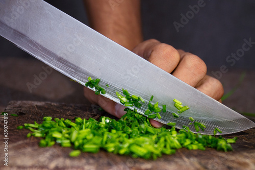 Foto Closeup shot of a man's hand slicing onion chives on a wooden chopping board