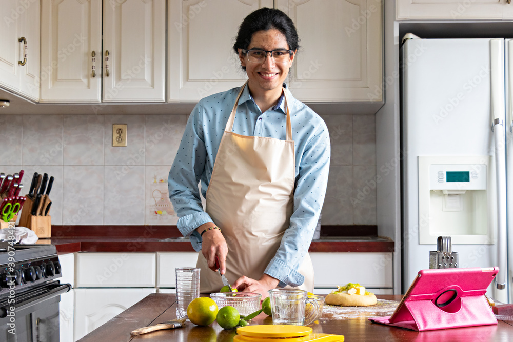 man in a kitchen, looking and smiling towards the camera, while cutting an orange man in a kitchen, looking and smiling towards the camera, while cutting an orange