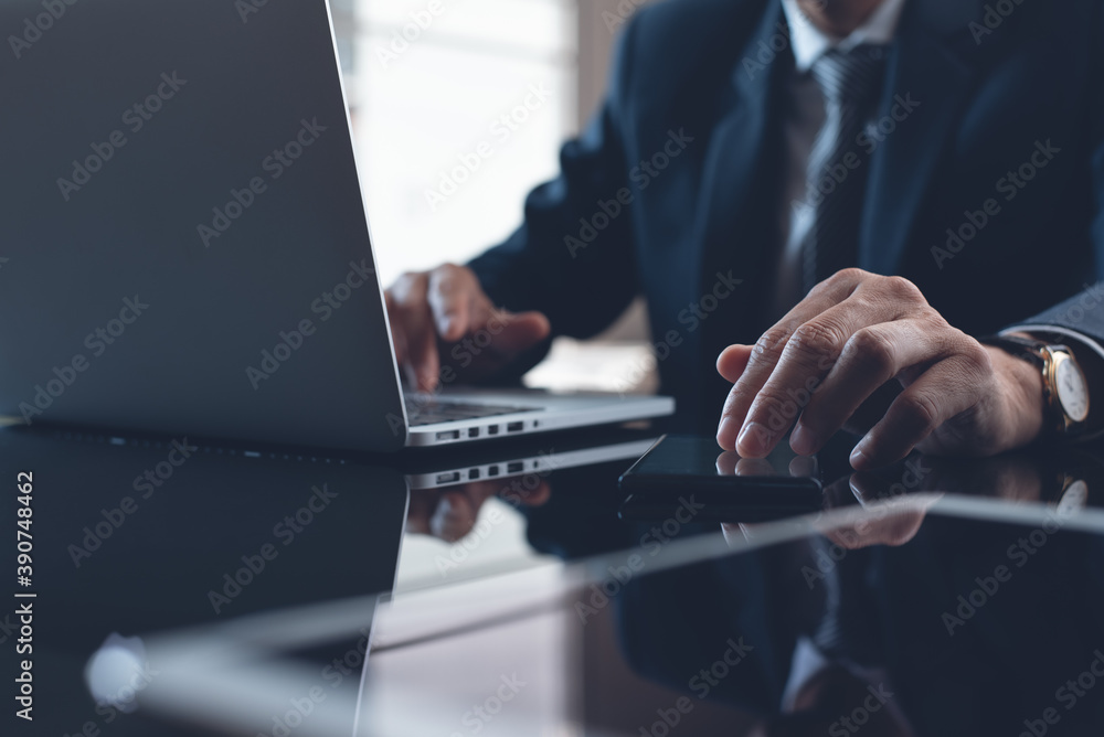 Businessman in black suit working on laptop computer and digital tablet in office Businessman in black suit working on laptop computer and digital tablet in office