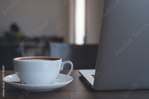 Cup of hot coffee and laptop computer on table in coffee shop with nobody for online working and telework concept