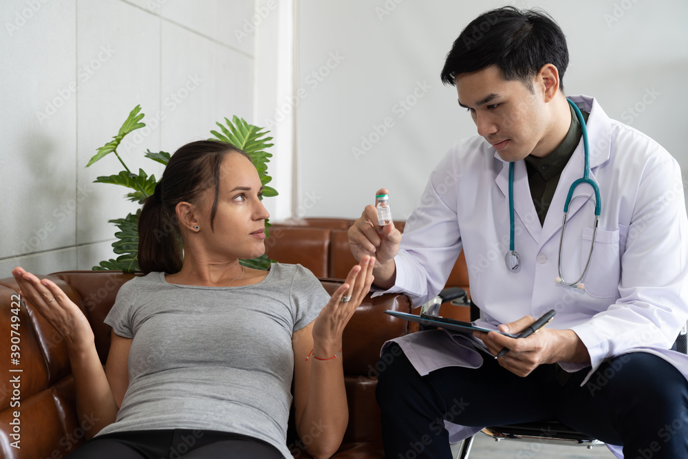 Fototapeta premium Asian male doctor holding medicine bottle while discussing to woman patient lying on sofa in the hospital or clinic. health, people and treatment concept