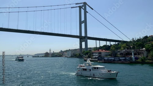 Footage of cruise tour boats and a yacht passing on Bosphorus strait in Kurucesme area of Istanbul. Bridge is in the view. Beautiful scene. It is a sunny summer day. Camera moves forward. photo