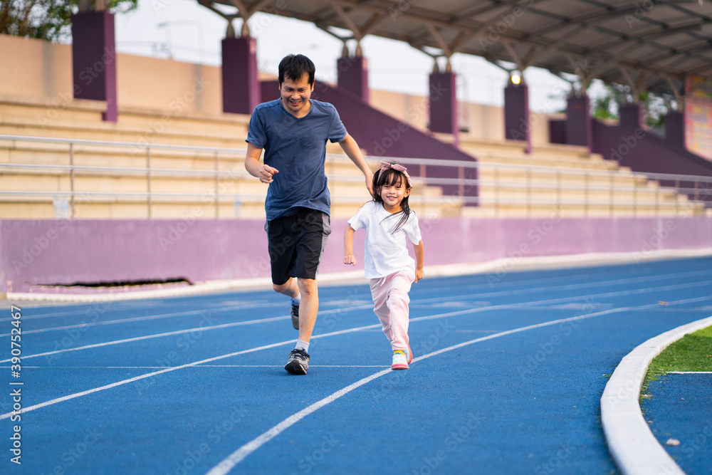 Fototapeta premium Asian little daughter is running in the stadium together with father, concept of outdoor activity, sport, exercise and competition learning for kid development.