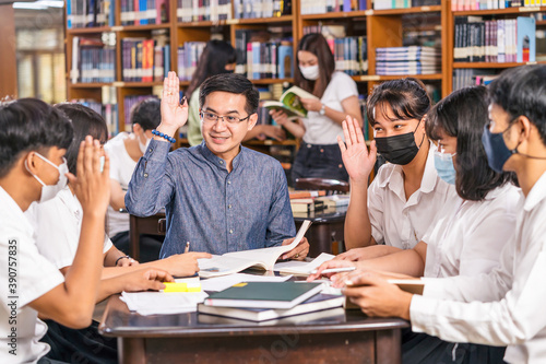 Asian teacher raising hand and Giving Lesson to group of College Students for answer question in the library and classroom, University education, back to school after reopen Covid-19 outbreak concept