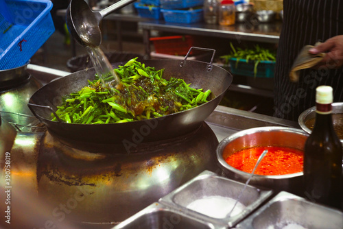 Motion Blur Chef's pours oil to cook kale in an Asian-style cast iron pan. Asia restaurant style menu. Stir Fried Kale with Salted Fish is favorite menu in Asian restaurants.
