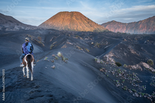 Bromo National Park, East Java, Indonesia - October 16, 2020 : Tengger man riding his horse on the black sand savanna of Mt Bromo, heading for Mt Batok photo