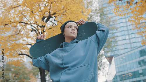 Young confident caucasian woman skater holding skateboard behind her head in the park in autumn. Low angle shot. High quality photo