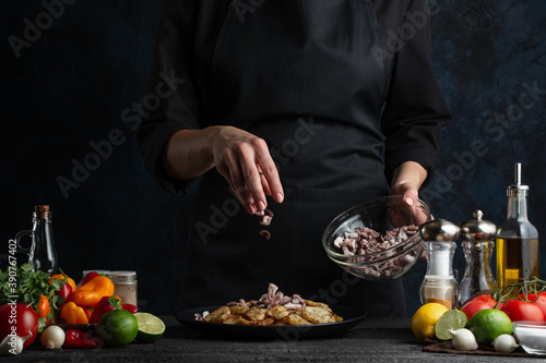 Professional chef in black uniform pours chopped octopuses on plate with baked potato. Concept of dinner with seafood. Traditional exotic asian cuisine.
