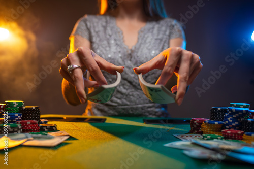 Woman shuffles poker cards in a casino on dark smoky background with lamps light. Concept of poker game. Frozen motion.