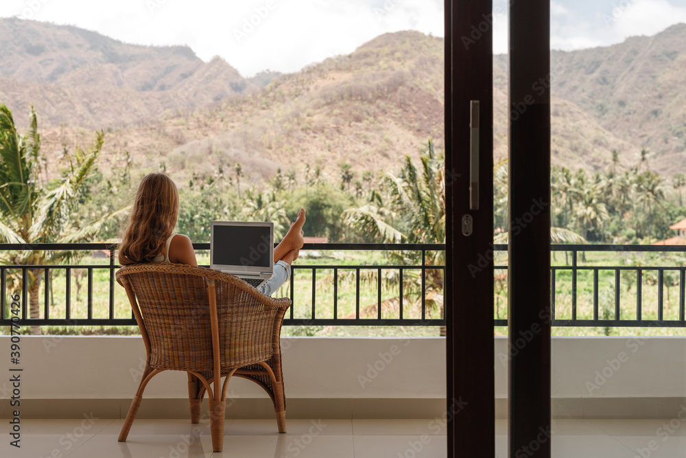 Back view happy confident woman using laptop while sitting on balcony and working from home Back view happy confident woman using laptop while sitting on balcony and working from home